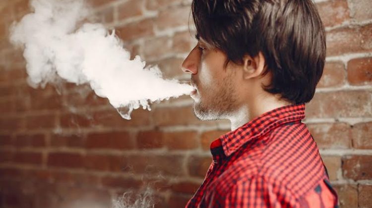 Stylish man in a city. Elegant male use the electronic cigarette