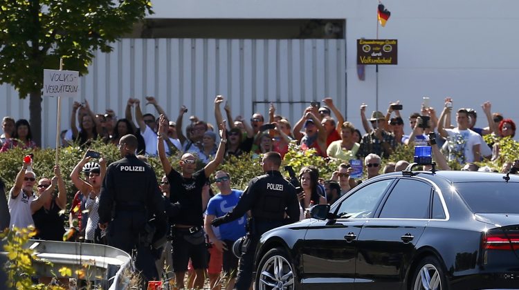 People hold a poster as Chancellor Merkel leaves after her visit to an asylum seekers accomodation facility in Heidenau