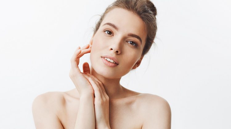 Beauty and health. Young good-looking skinny caucasian girl with dark hair in bun hairstyle being naked, looking in camera with relaxed and happy expression, touching hand with hands, feeling refreshed after spa treatments